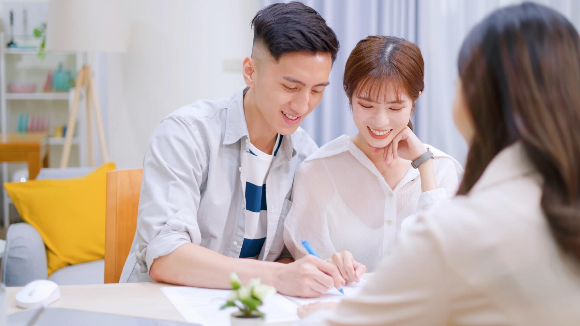 Happy couple signing paperwork with office colleague